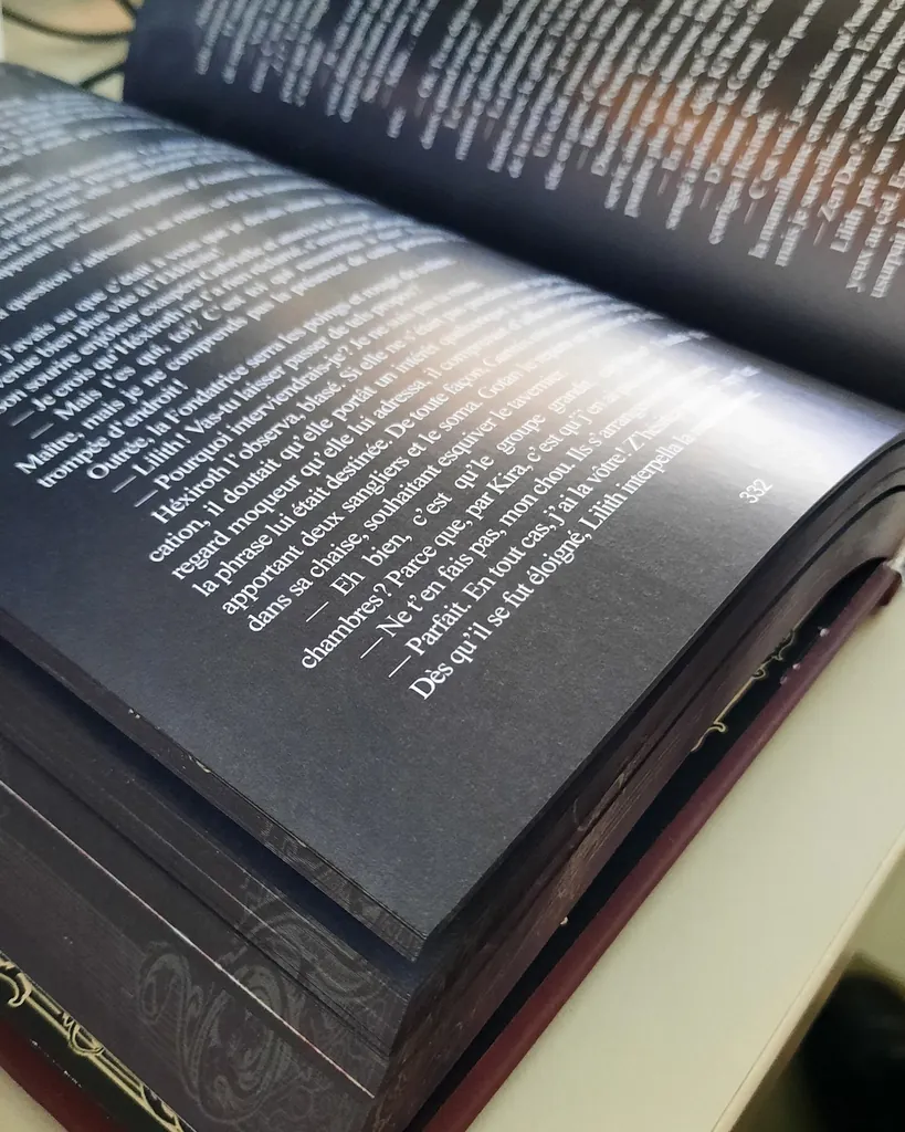 Livre à couverture rigide ouvert, toutes les pages imprimées en blanc sur papier noir, tranches sombres ornementales et couverture bordeaux avec dorure
